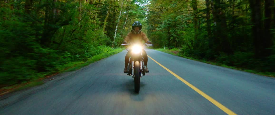 A motorcycle travels on a rural road with its headlight on