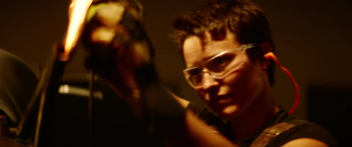 A woman with short hair uses a power tool to grind and smooth a piece of metal