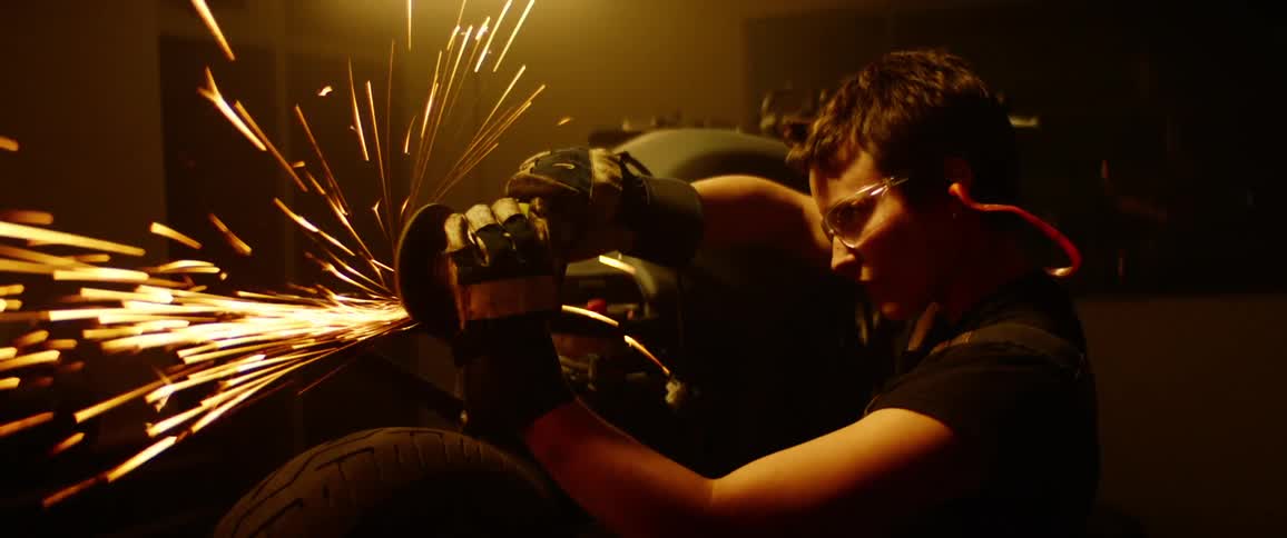 A female mechanic uses an angle grinder on the chassis of a motorcycle in a garage at night