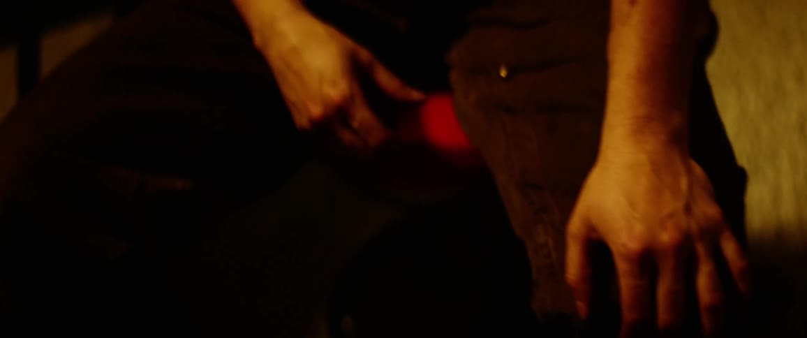 A man sits in a dimly lit area still with his hand placed on his knee
