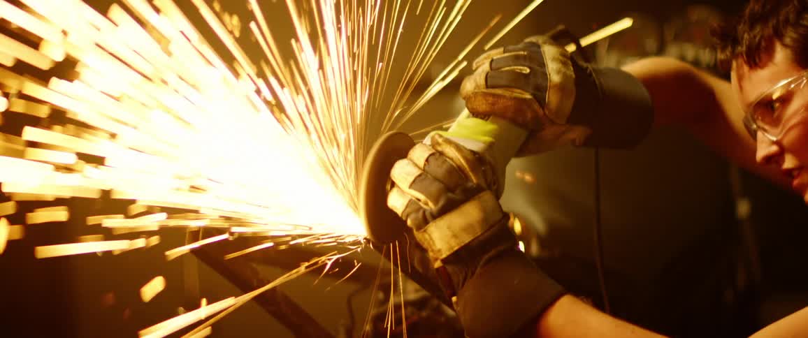 Woman grinds metal frame with power tool while wearing safety goggles and gloves