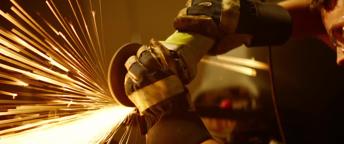 A person with goggles and headphones using an electric grinder with sparks