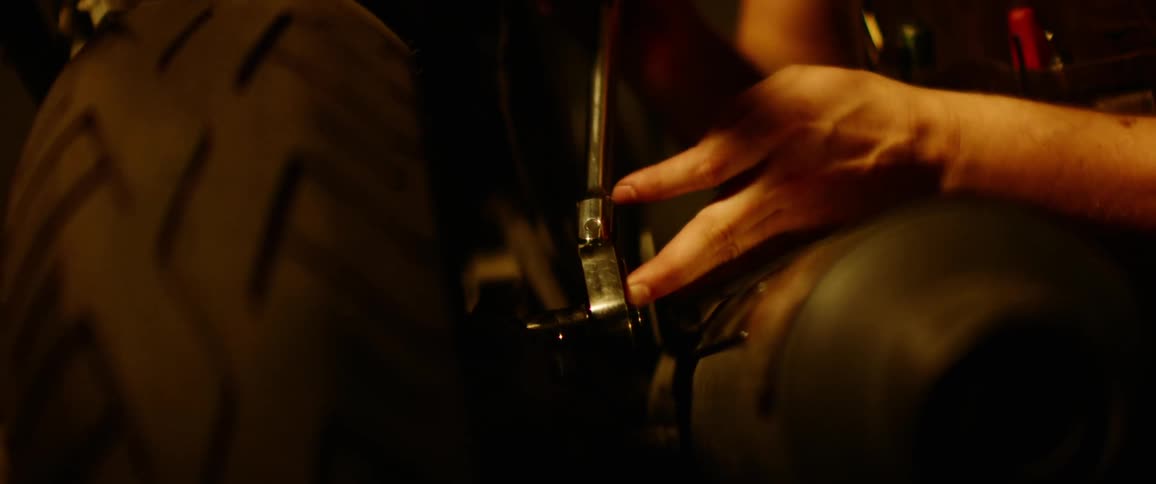 Person uses socket wrench on large wheel wearing apron with pens in chest level pockets