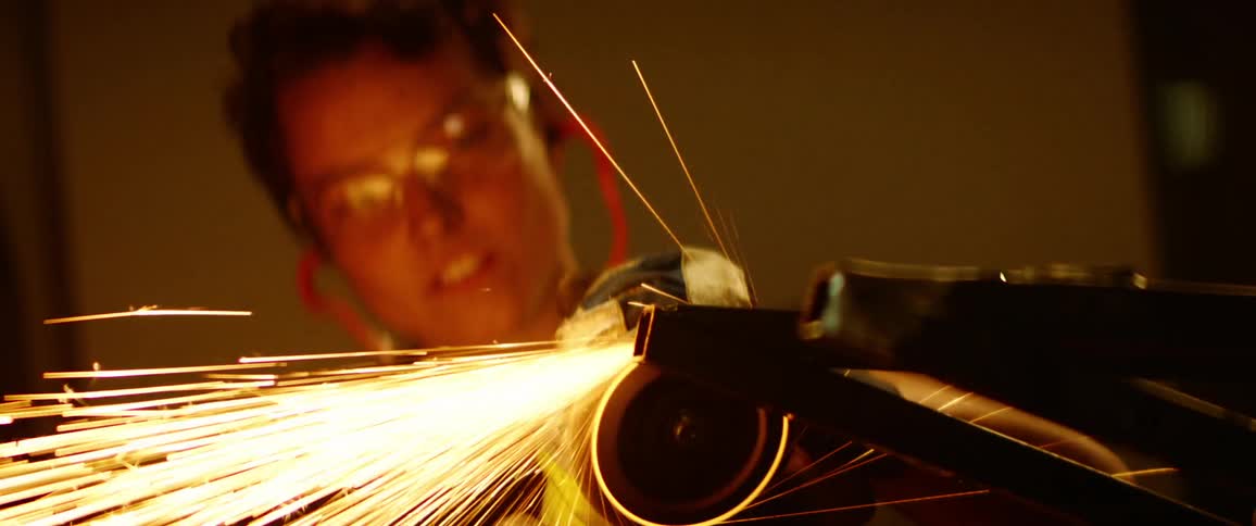Woman grinds metal motorcycle frame creating a shower of sparks