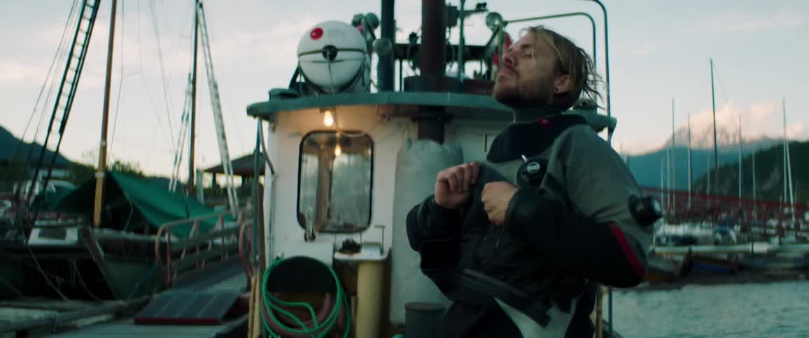 Young bearded man puts on a jacket aboard a fishing boat in a pier at sunrise