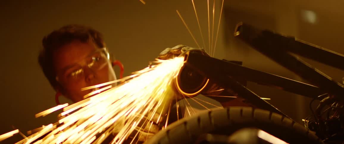 Female mechanic uses a power tool to grind the frame of a motorcycle in a dimly lit workshop