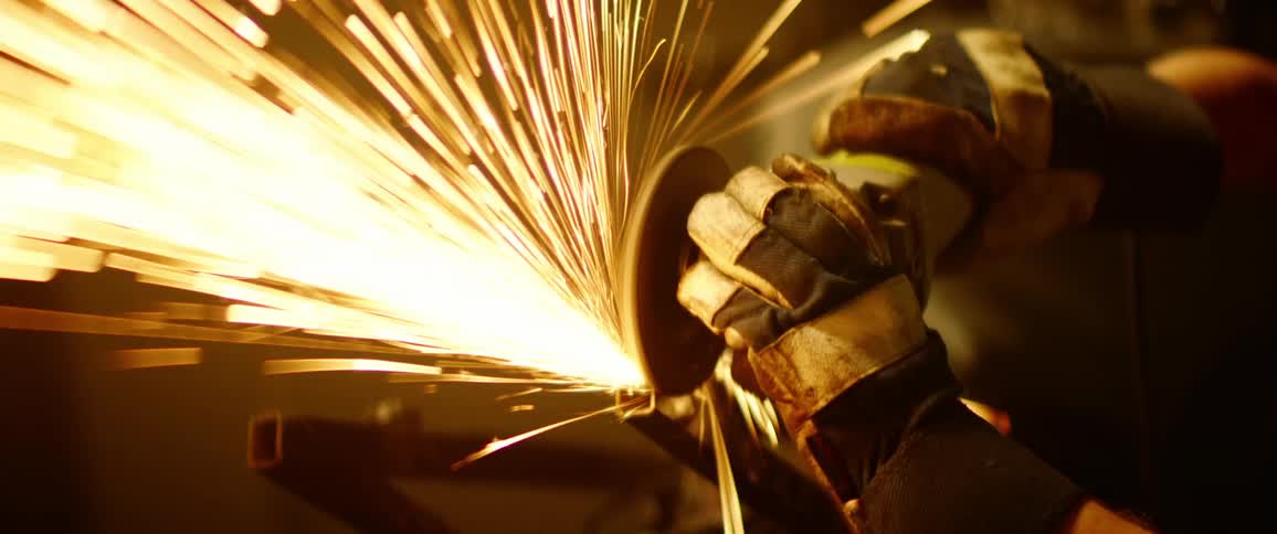 A person with an electric grinder and goggles grinding metal with sparks