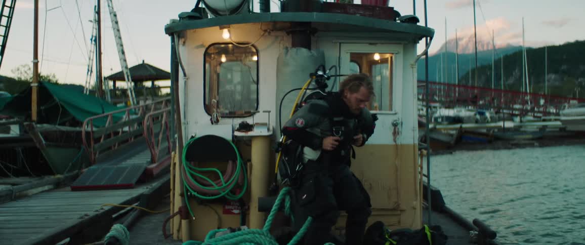 A man standing on a boat in a marina putting on an oxygen tank on his back