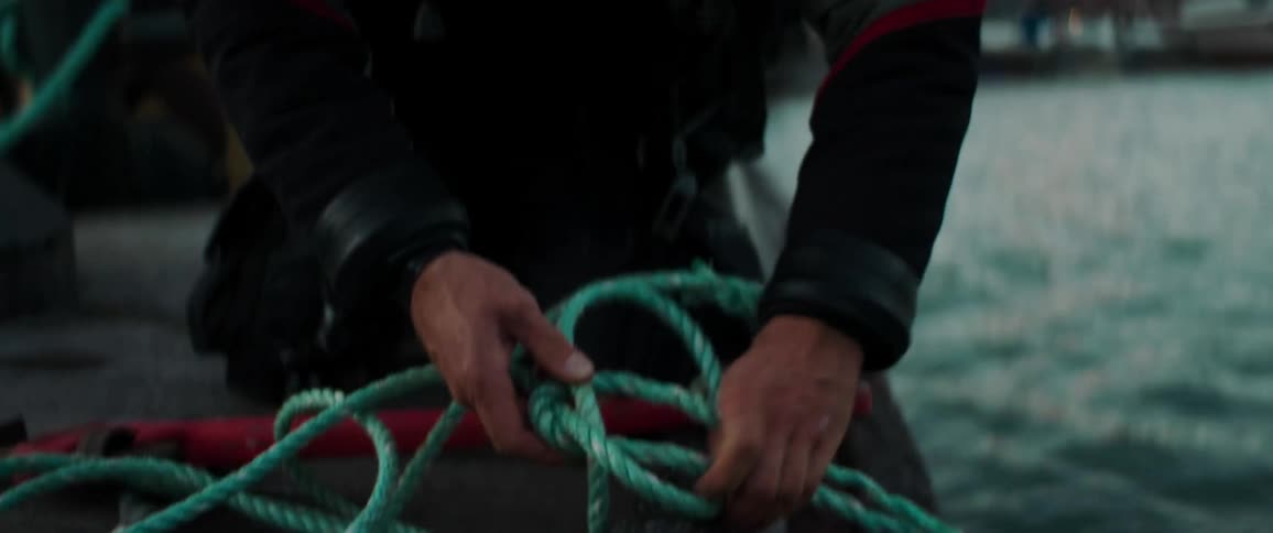 A man kneels on a boat tying a rope to it