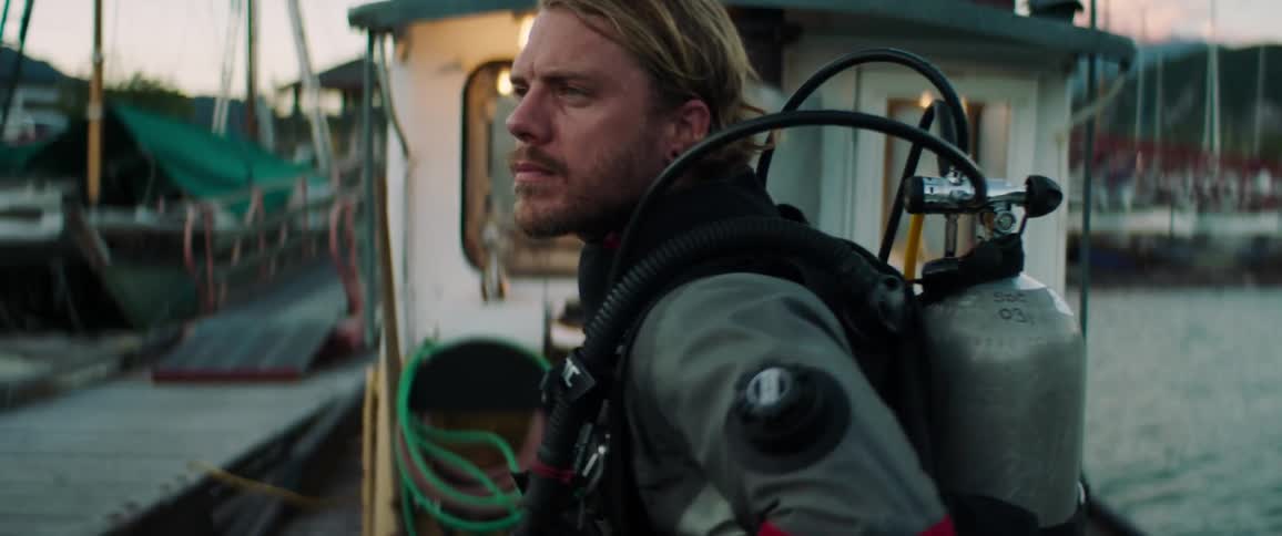 A man stands on a docked boat wearing scuba gear
