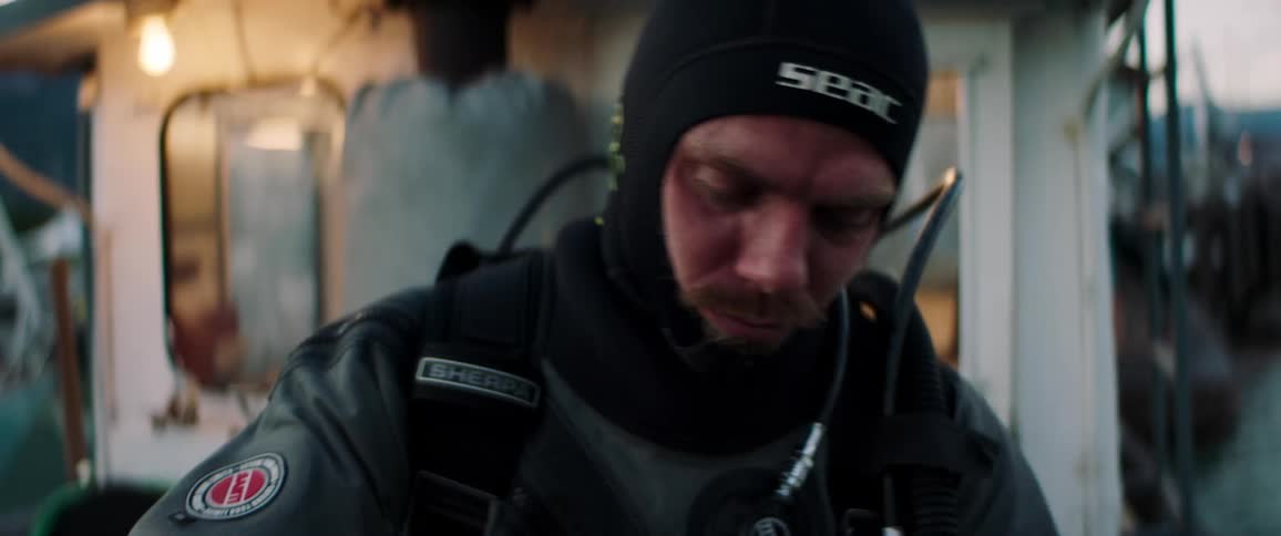 Man dons scuba equipment on boat near dock as water ripples between boat and pier