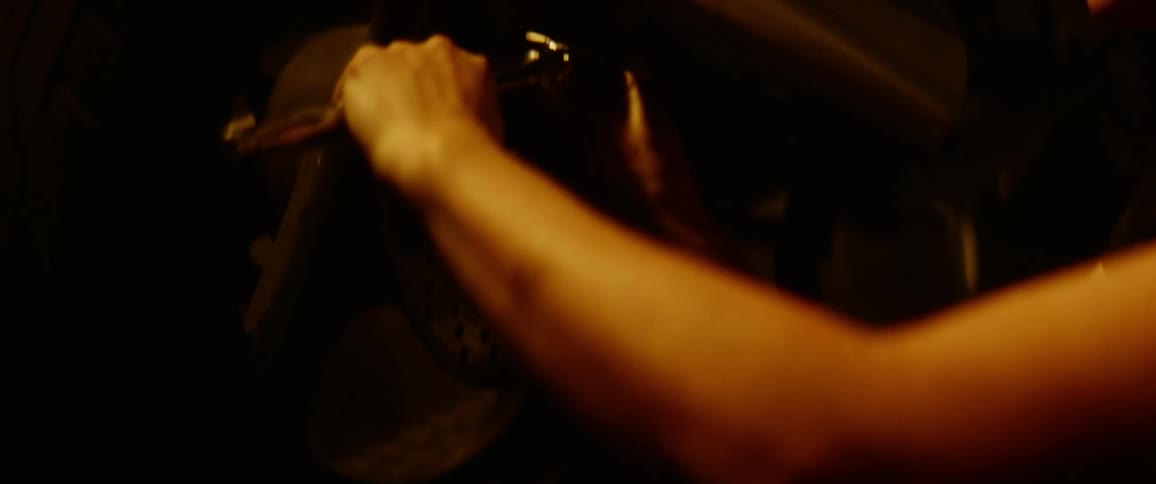 A woman working on her motorcycle turns around in her stool to grab a wrench