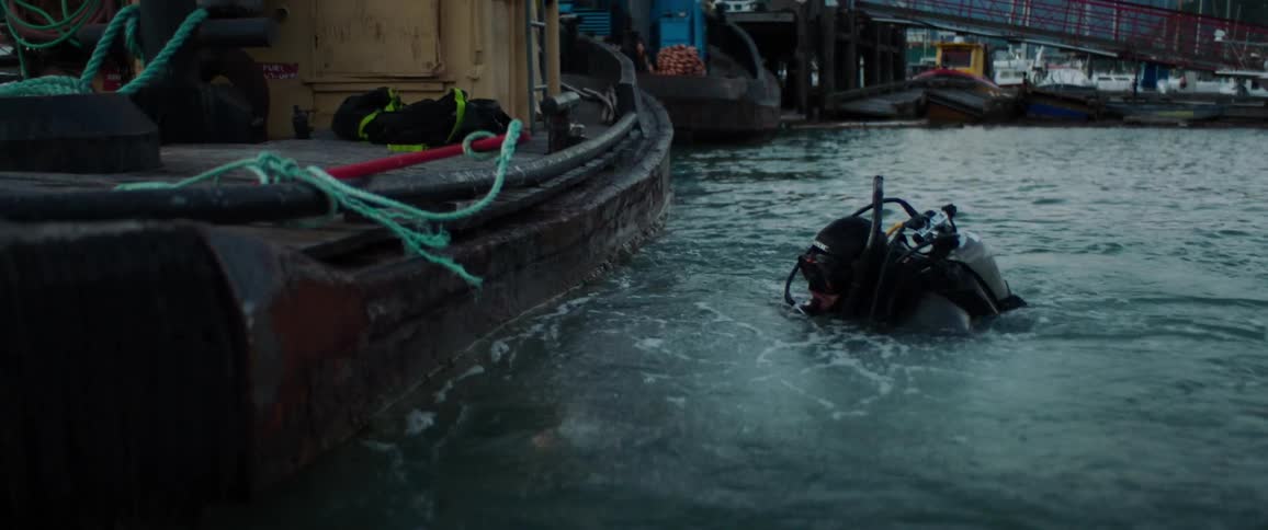 A person in full scuba gear jumps off of a marina parked boat into the water and grabs a tool attached to a rope