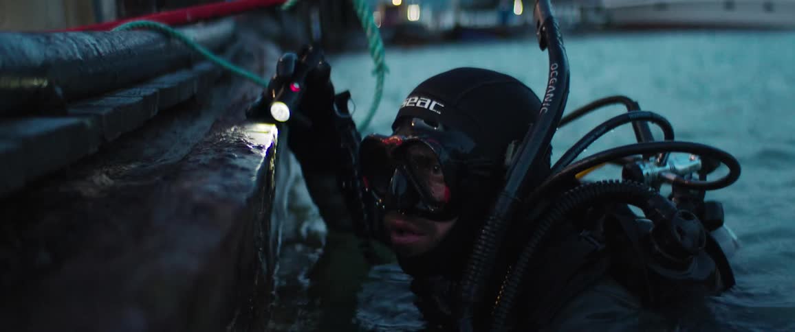 A scuba diver with his head above water shines his flashlight on the dock