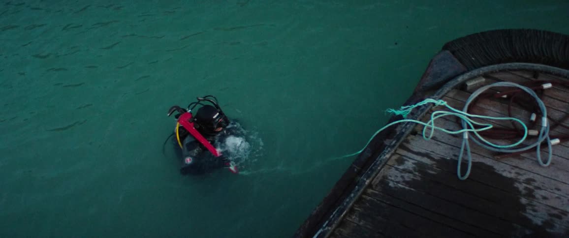 A person in full scuba gear appears out of the water and places a tool on a boat beside them