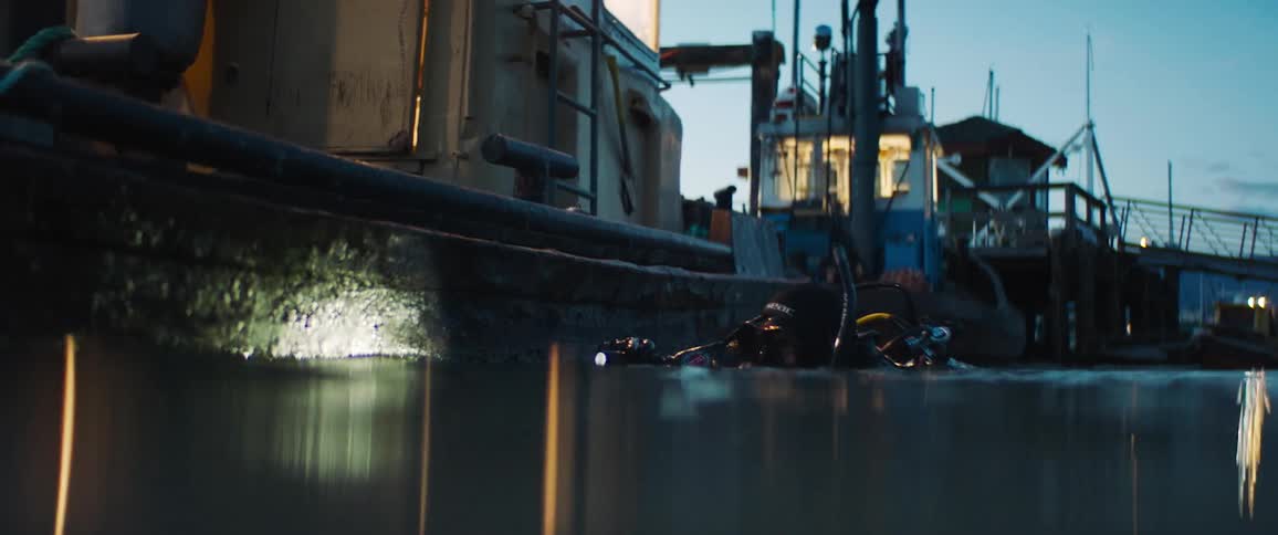 A diver swimming near a boat examines the hull with a flashlight