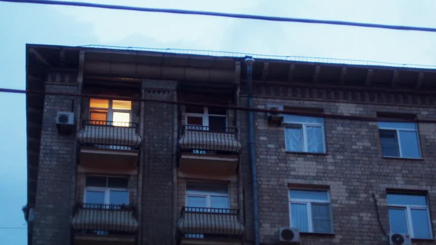 Light shines from apartment in upper corner of building towering over tree and powerlines