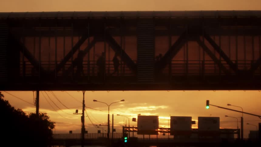 Pedestrians cross over busy highway on pedestrian bridge under a red tinted sky