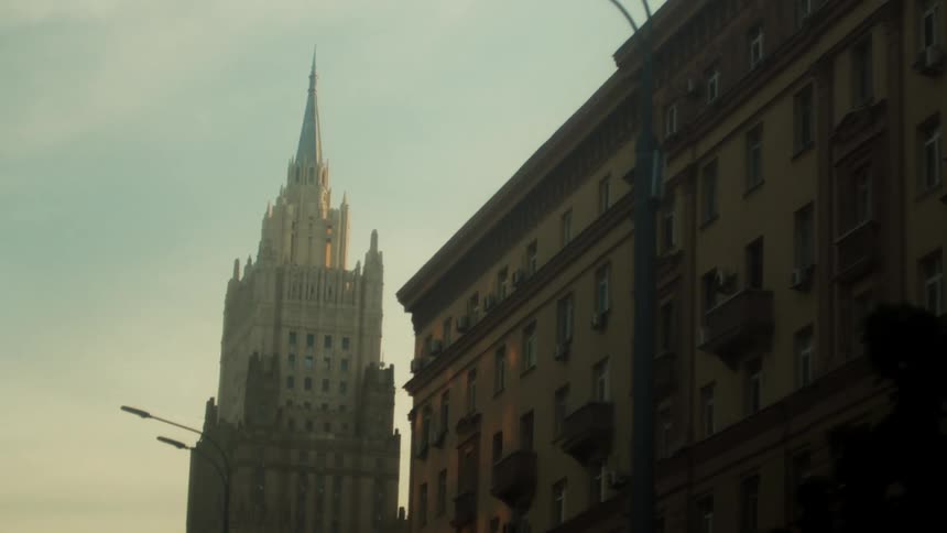 A wide apartment building sits next to a tall skyscraper with a pointed spire