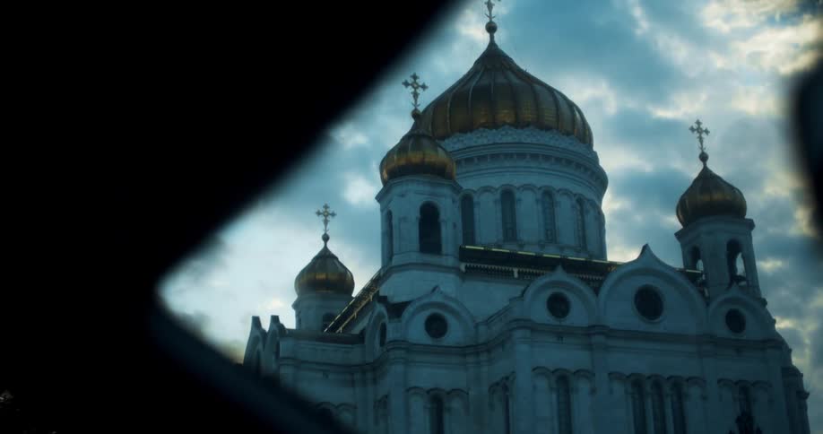 Vehicle drives past ornate domed church under cloudy sky