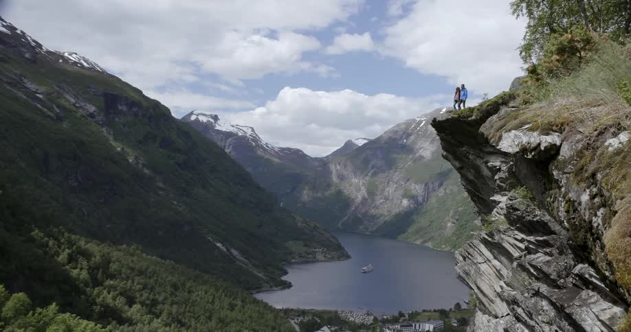 A man and woman standing on a cliff overlooking a body of water in a mountain valley
