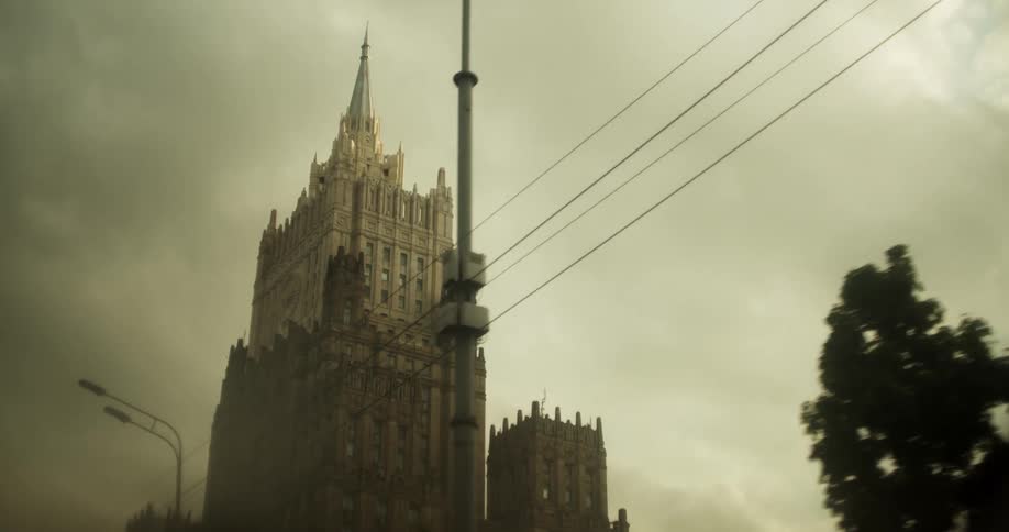 A gothic style building sits off a tree lined road in a city
