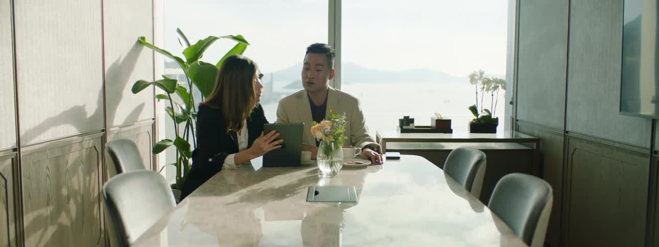 A man and woman in a conference room look at a tablet together