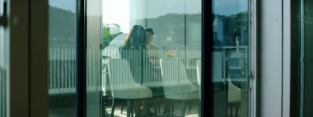 A man and woman walk into a conference room with floor to ceiling windows and sit down to talk