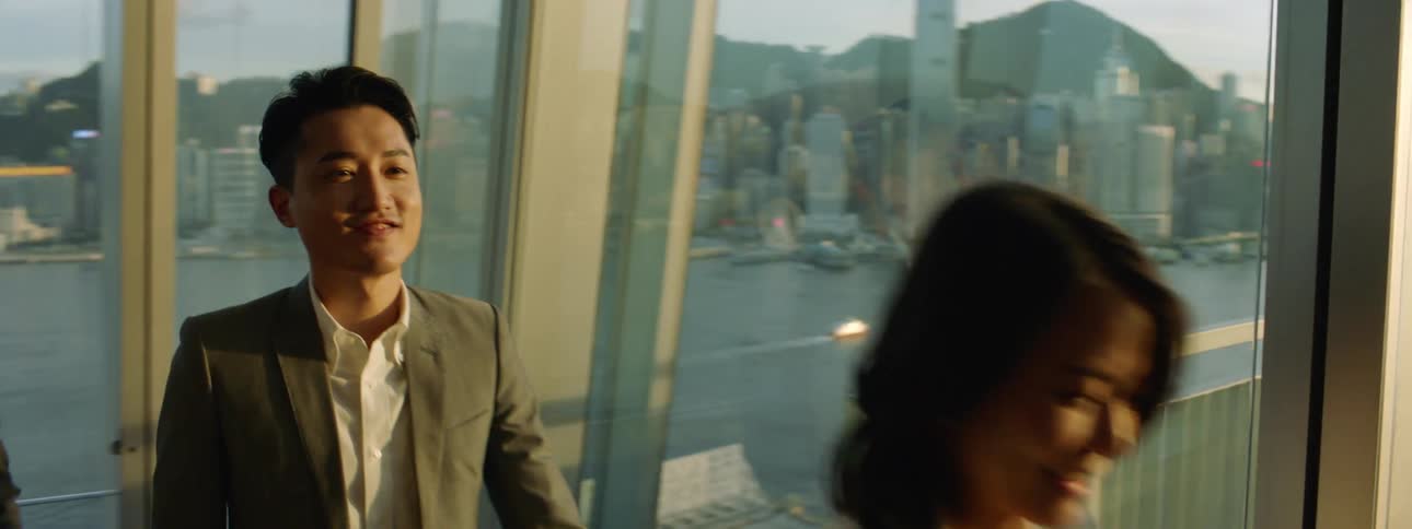 A group of asian men and women in formal business clothing walk together through a highrise overlooking the bay of a metropolis during the day