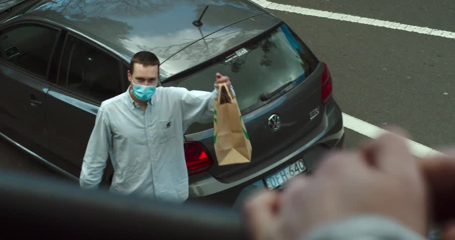 A man waving and holding up a grocery bag on the street