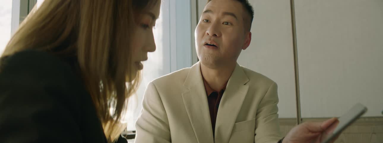 A man and woman sit at an office table talking about what they see on a tablet