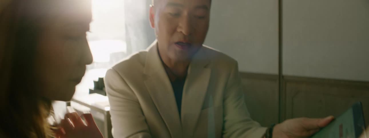 A man hold a tablet computer while talking to a woman sitting at the table with him