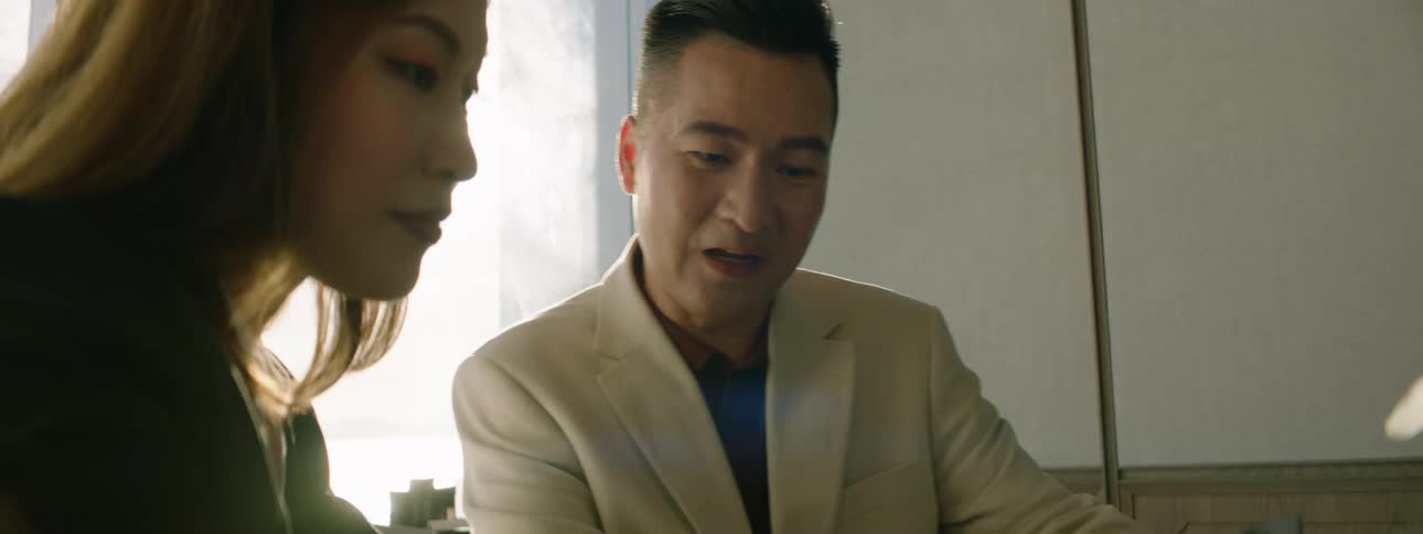 An asian man and woman sitting at a table in a restaurant speak while looking at a tablet together
