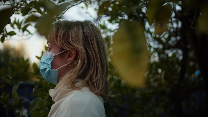 A woman is standing outdoors and wearing a mask