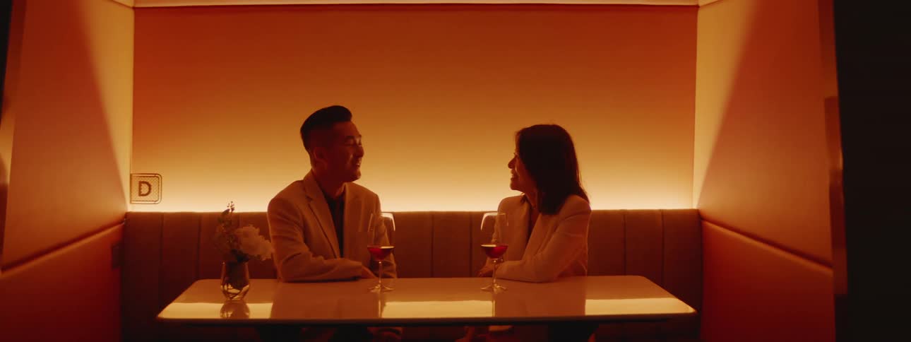 A man and woman speak while sitting in a booth in a club