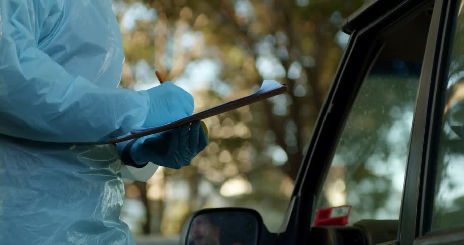 A woman with a mask face shield and gloves writing on a paper on a clipboard
