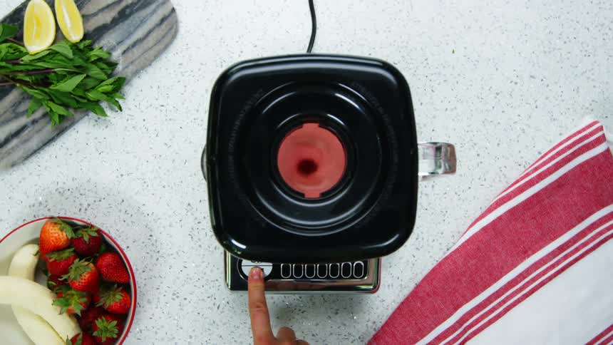 Person turns on and turns off blender sitting on counter near bowl of fruit and chopping board