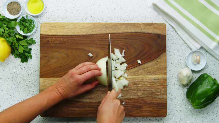 A person dices a onion on a wooden cutting board