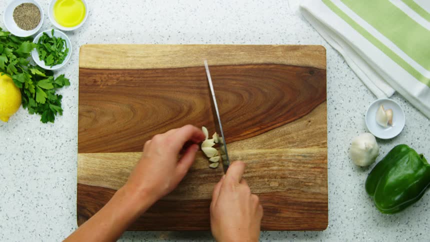 A person cutting garlic on a cutting board with a knife