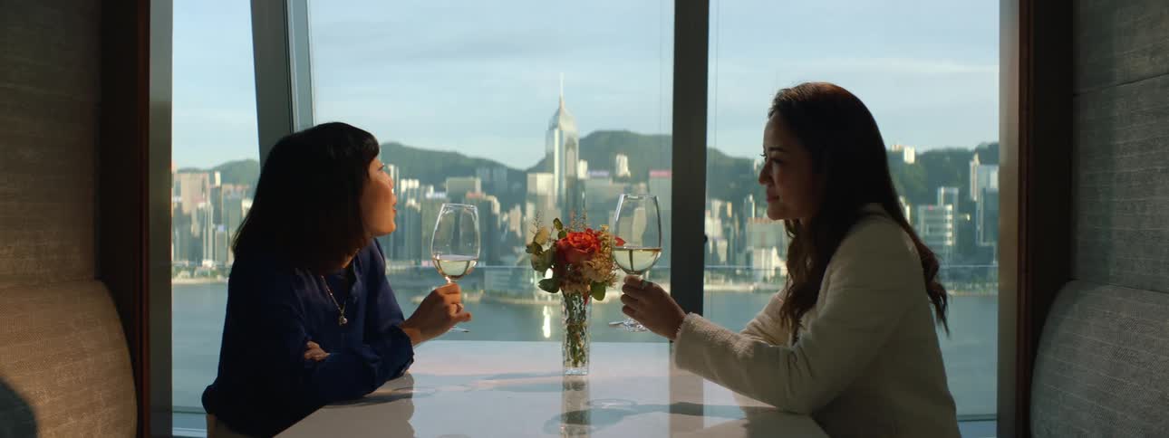 Two women sip on a glass of wine in a restaurant with a view to the city and lake