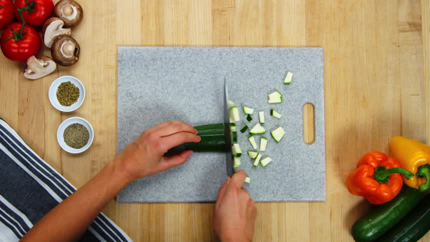 A woman cuts cucumber into small chunks on a gray cutting board