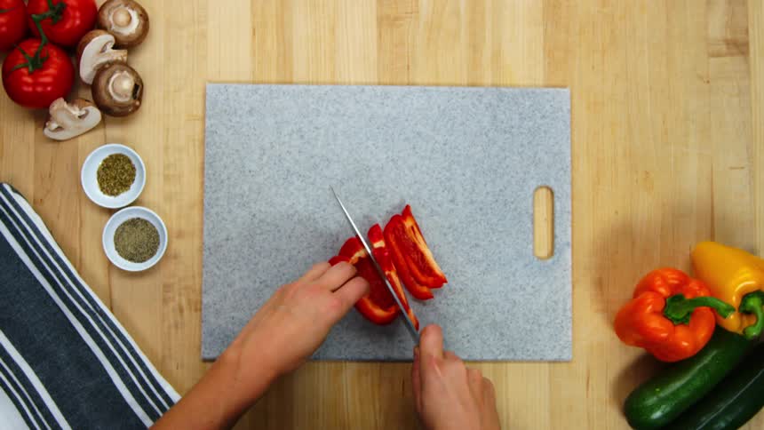 A cook slices a red bell pepper on a cutting board