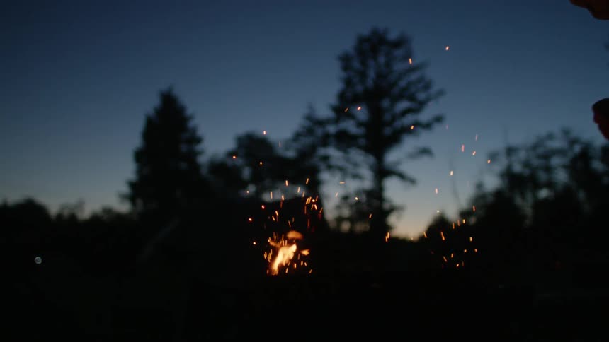 A person is standing by a bonfire at night