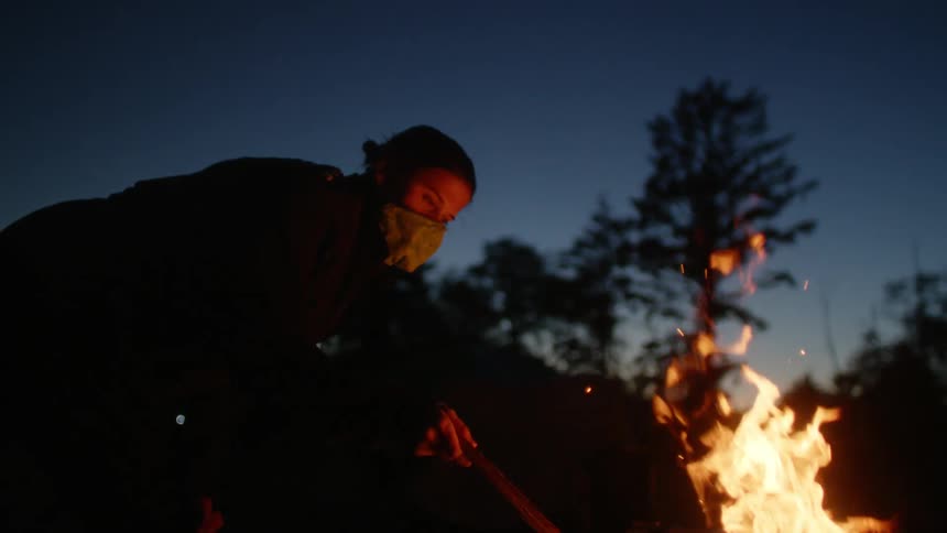 A woman is standing by a bonfire at night