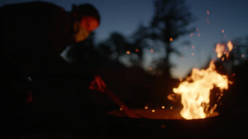 A woman is by a bonfire at night