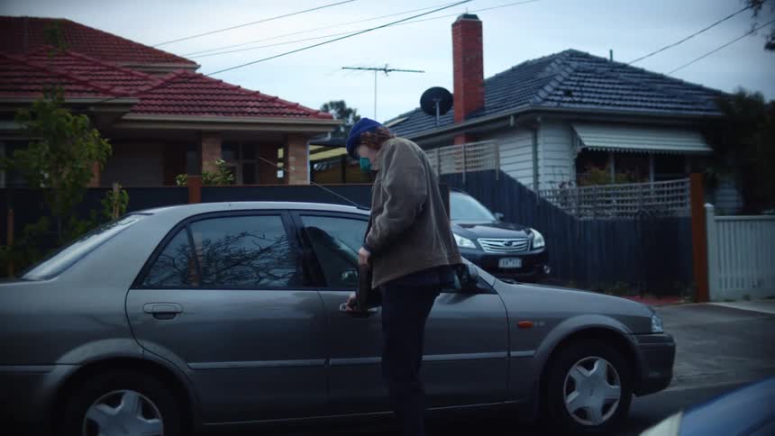 A man walks to a parking lot in a city neighborhood before unlocking and climbing into a vehicle