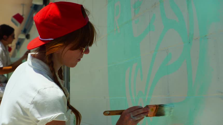 Two women paint pictures on the building