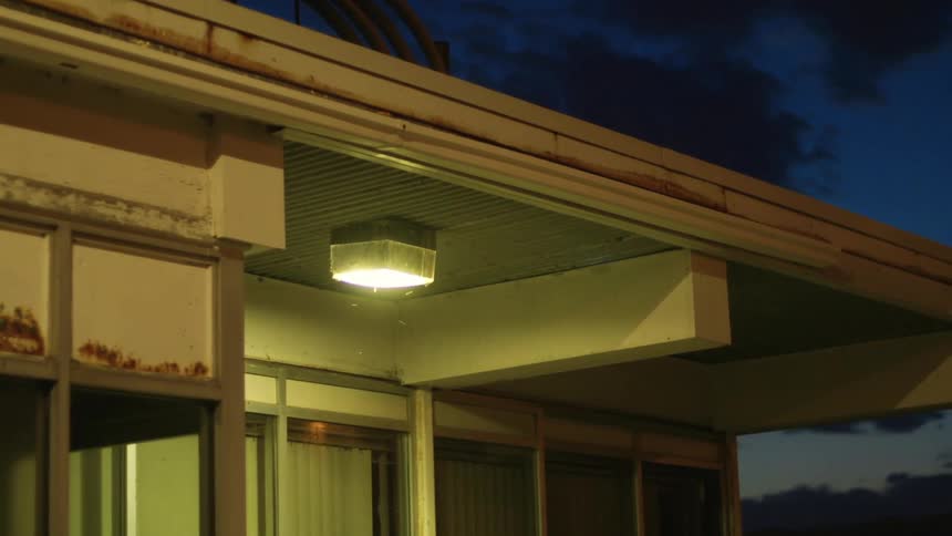 Insects flying around an illuminated porch light on a building at night