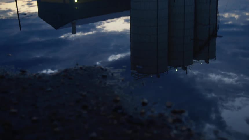 A puddle of water reflecting a building silos the sky and clouds