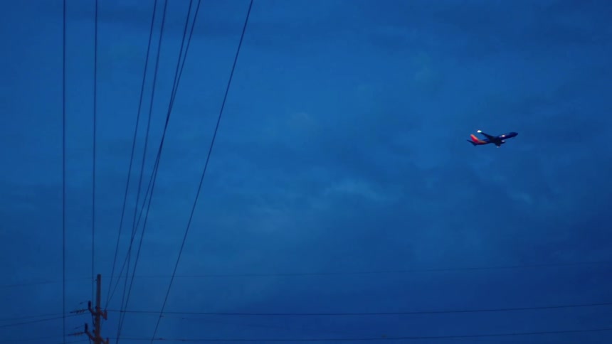 An airplane flying with a utility pole in the foreground and the sky and clouds in the background